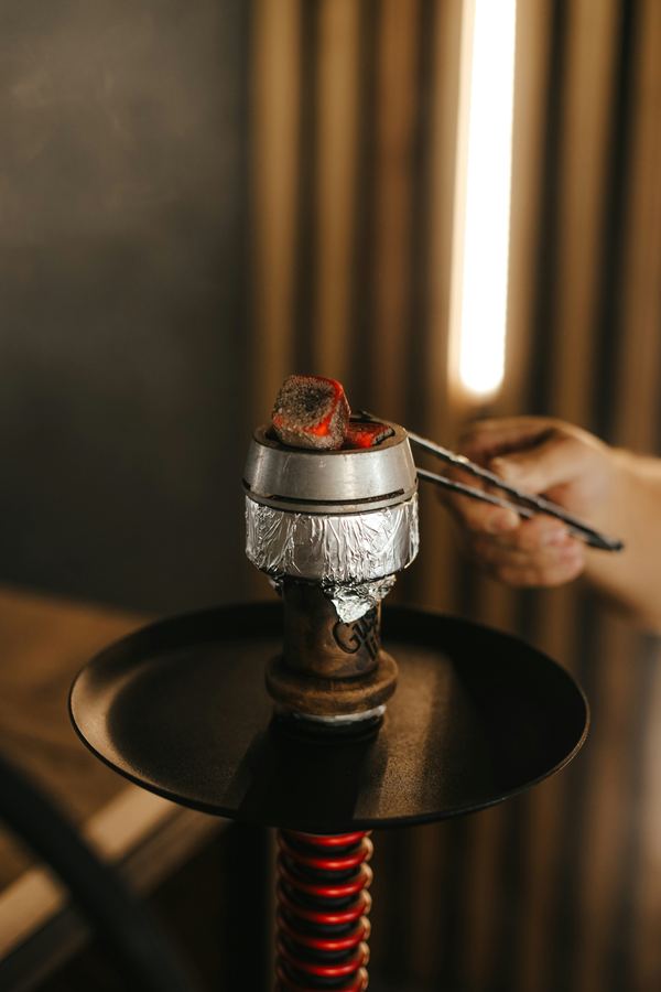 Hot coals being placed on a hookah bowl with tongs